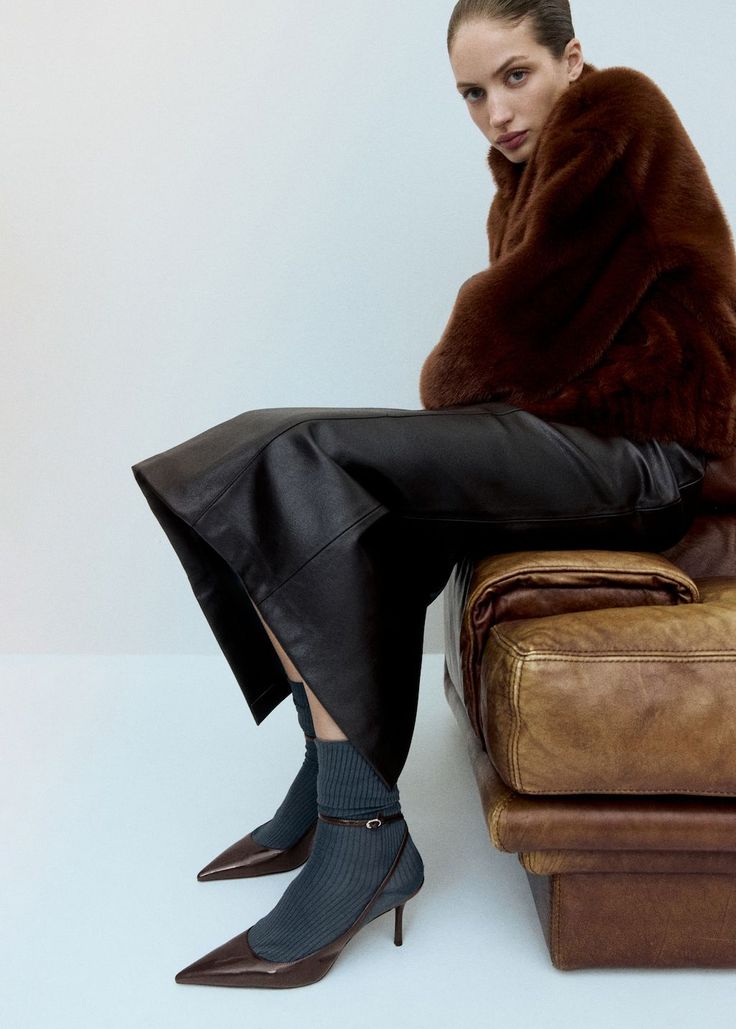 Woman in a brown fur coat and leather skirt sitting on a leather couch