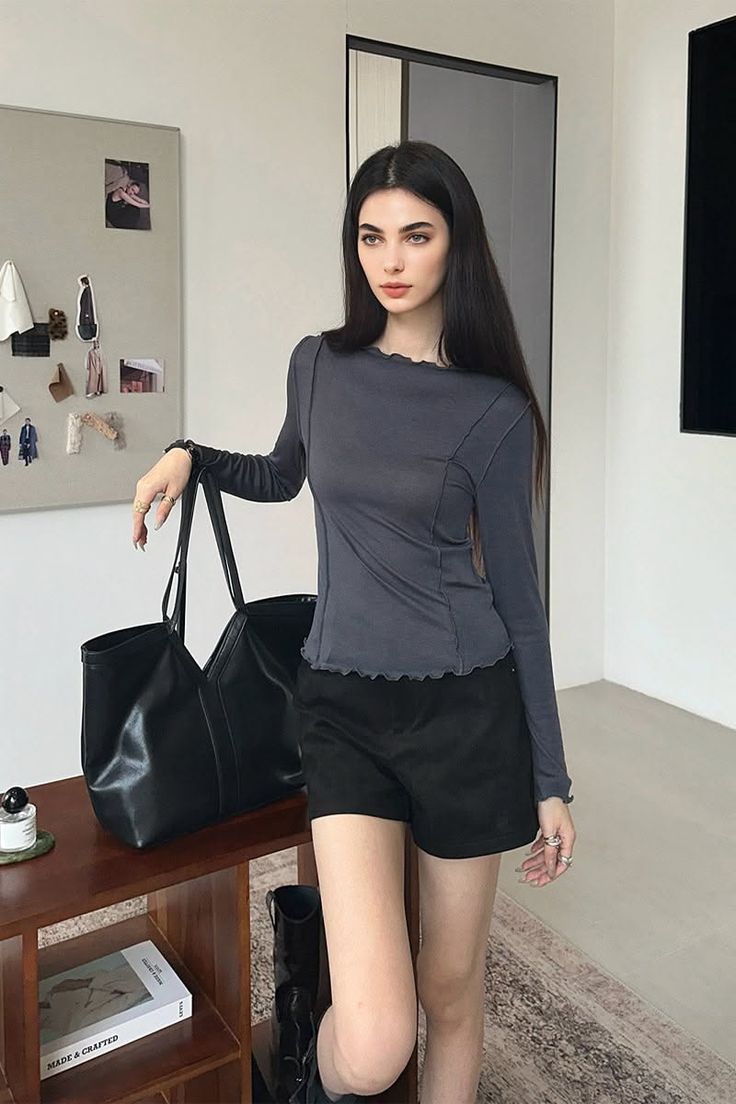 Woman with long black hair wearing a long sleeve top and black shorts indoors