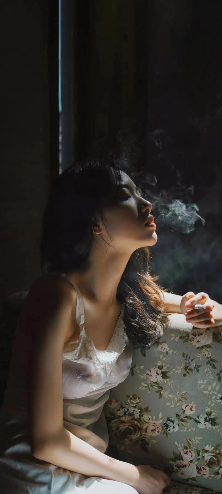 Woman in a white slip dress smoking indoors with dramatic lighting