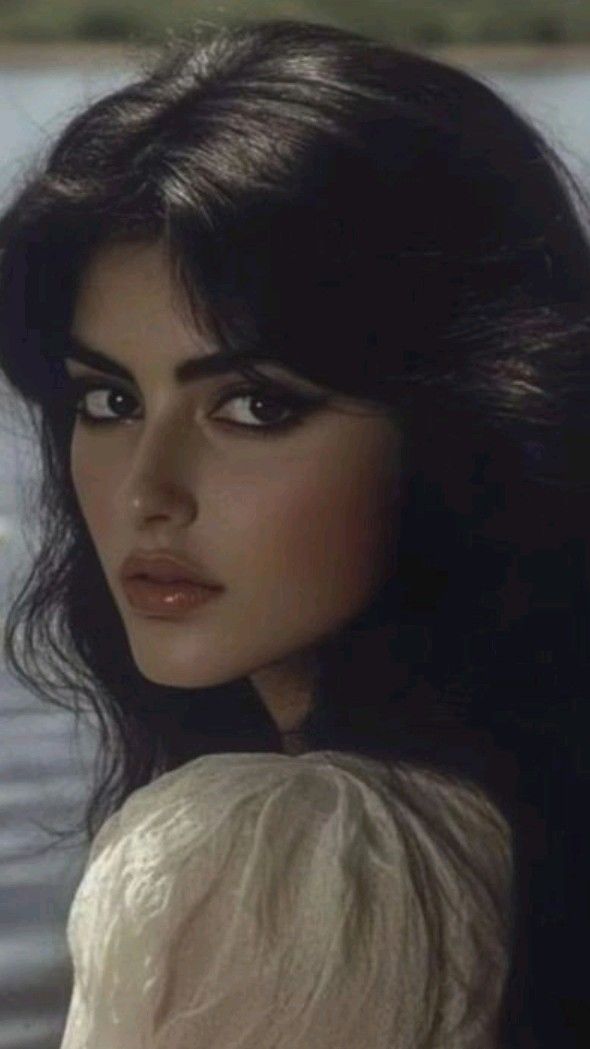 Woman with dark hair and makeup looking over her shoulder outdoors