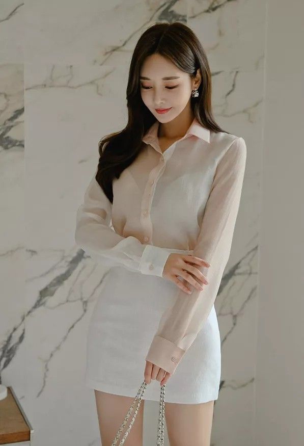 Woman in a white sheer shirt and white skirt holding a bag indoors
