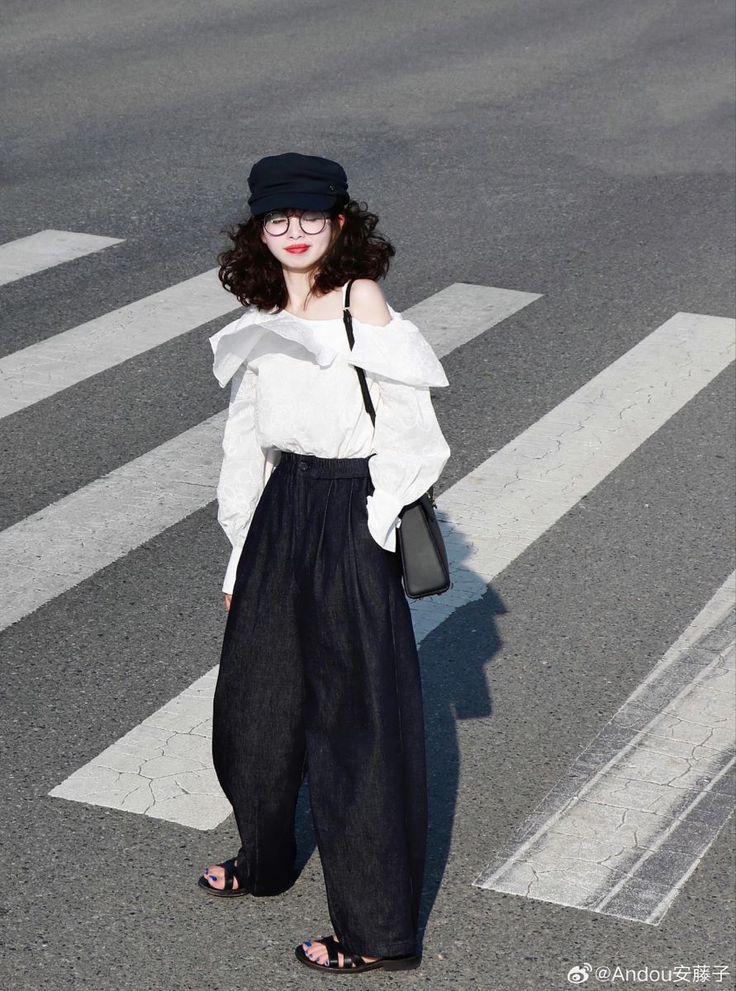 Woman with curly hair wearing a white blouse and wide-leg pants on a crosswalk