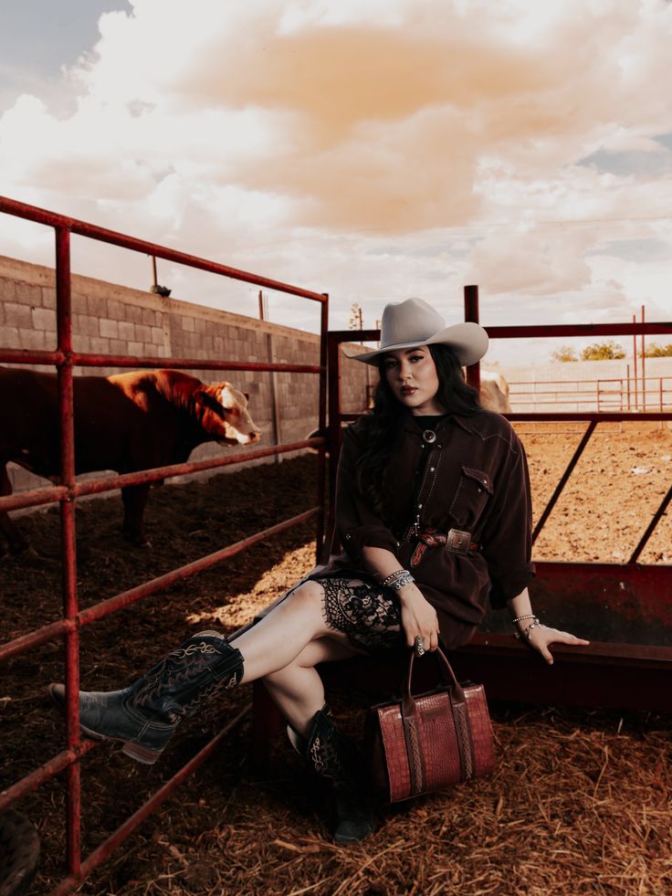Woman in a cowboy hat and boots sitting on a fence at a farm