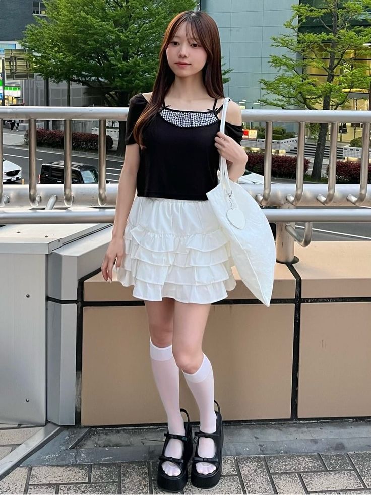 Woman with long hair wearing a black top and white ruffled skirt outdoors