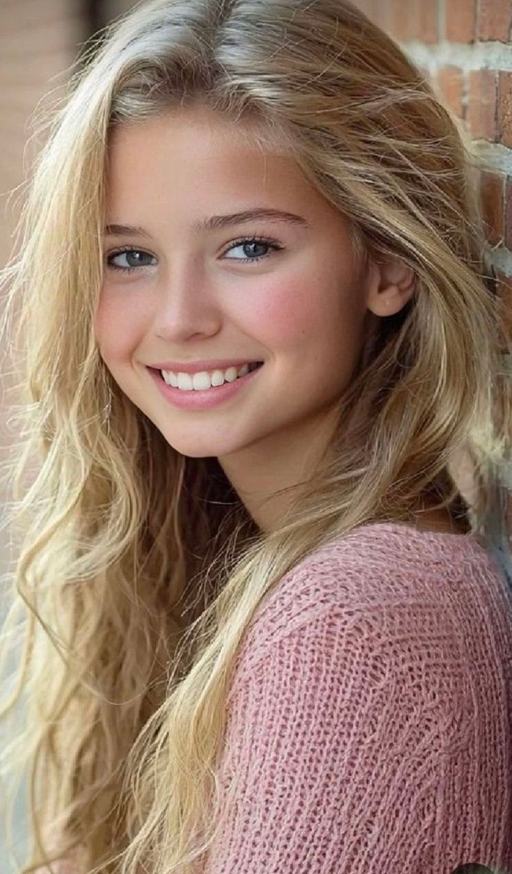 Young girl with blonde hair and a pink sweater smiling at the camera