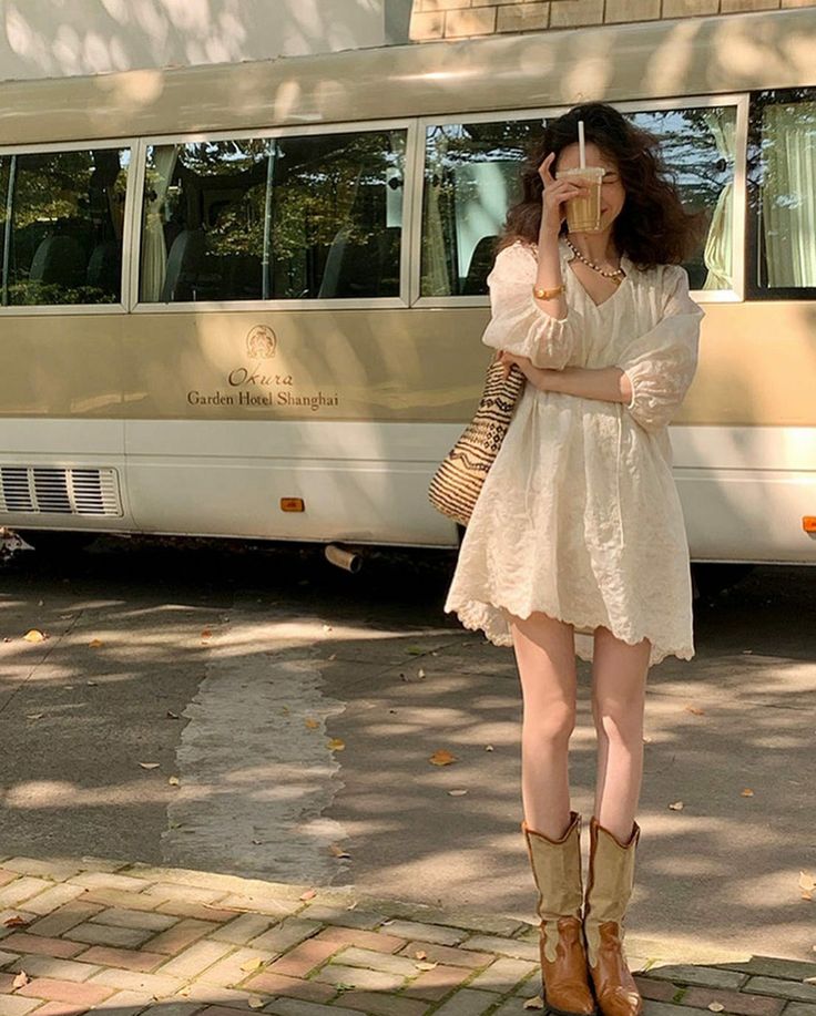 Woman in a white dress and cowboy boots holding a drink outdoors