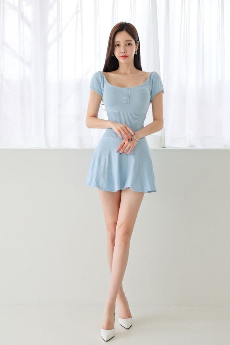 Woman in a light blue dress and white heels standing indoors