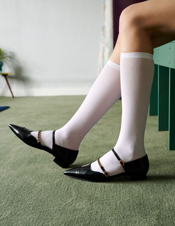 Person wearing white knee-high socks and black shoes with gold chains on a green carpet