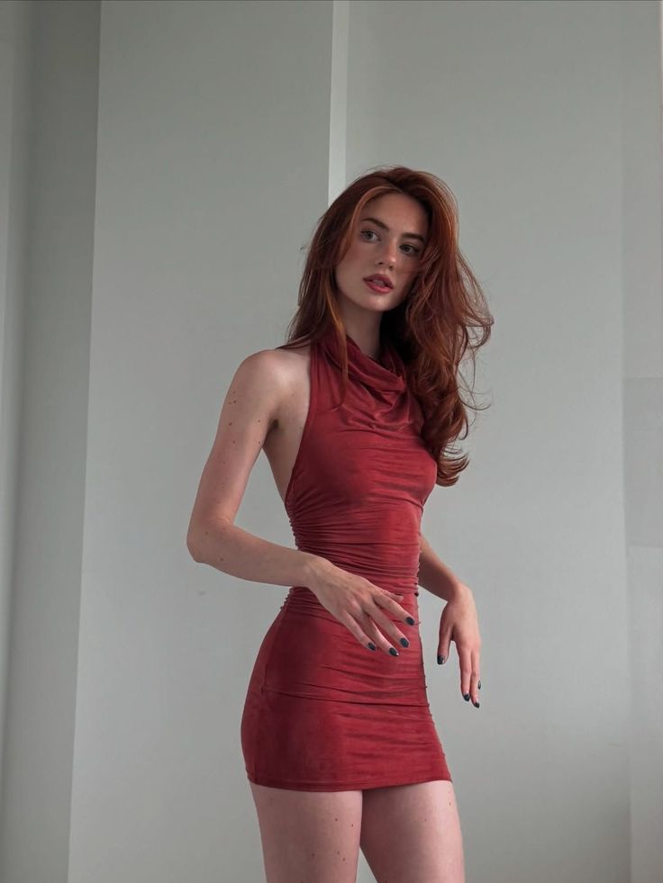 Woman with long red hair in a tight red dress posing indoors