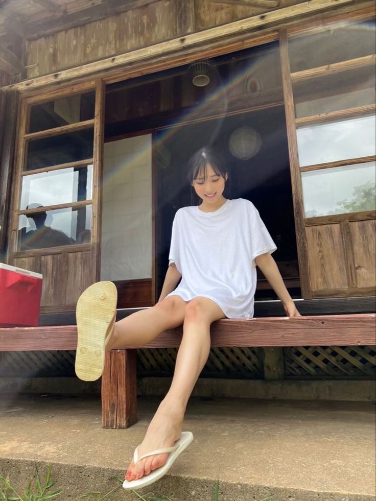 Woman in a white t-shirt and flip flops sitting on a wooden porch