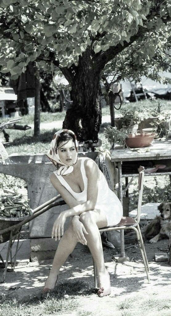 Woman in a white dress and head scarf sitting outdoors with a dog nearby