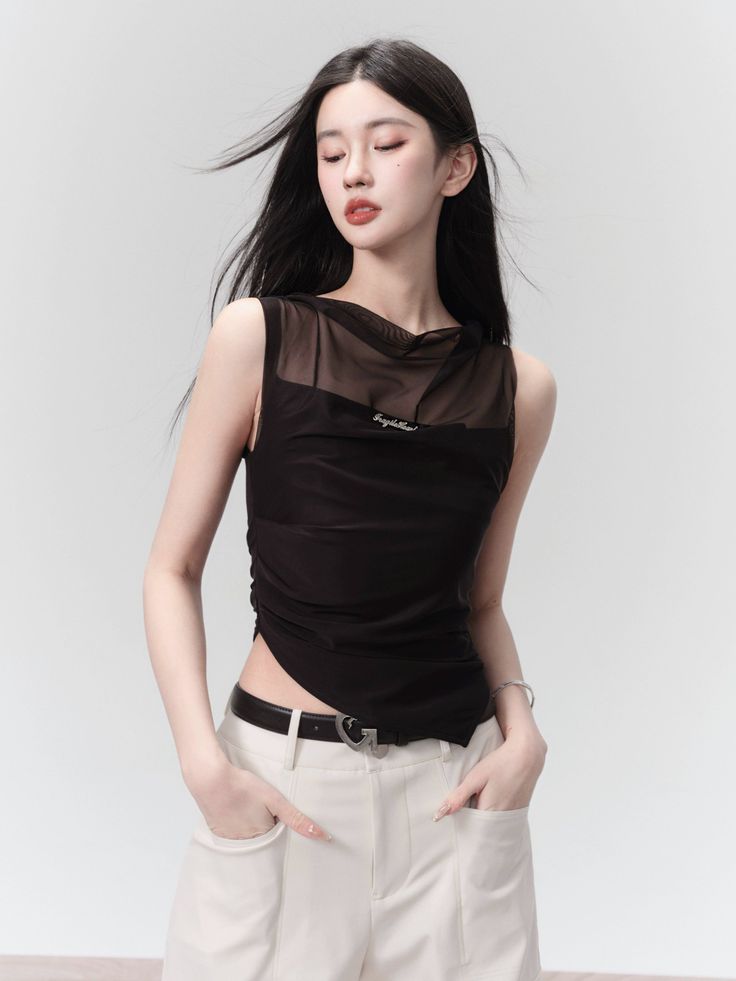 Woman with long black hair wearing a sheer black top and white pants in a studio