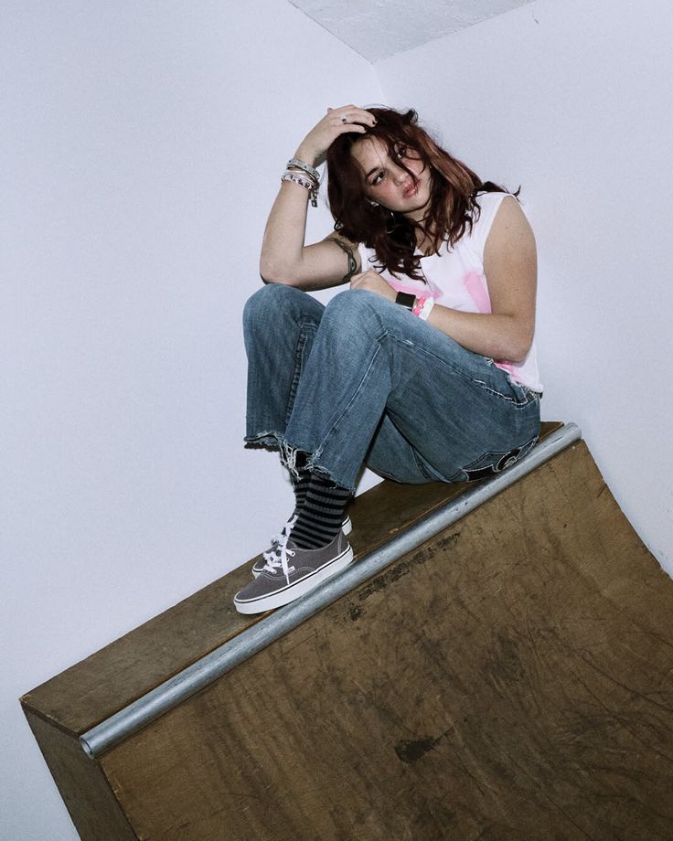 Person with long hair and jeans sitting on a wooden ramp indoors