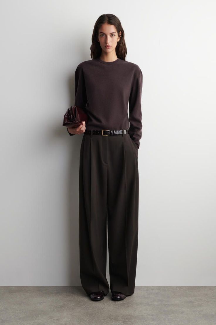 Woman in a dark brown sweater and wide leg pants holding a clutch bag