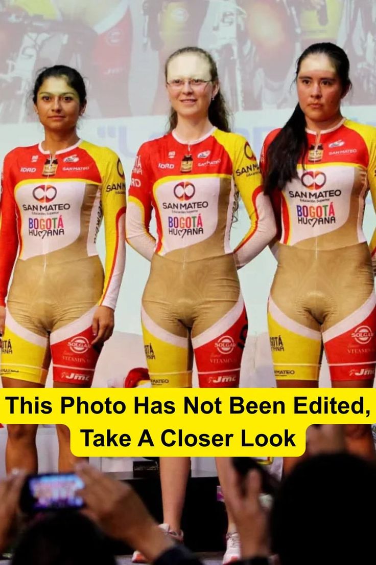 Three women in tight cycling uniforms on a stage with an audience taking photos