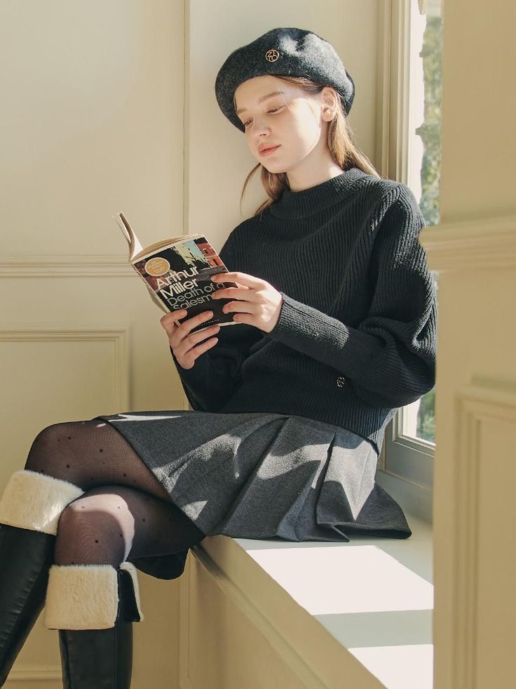 Woman in a beret and sweater reading a book by a sunlit window