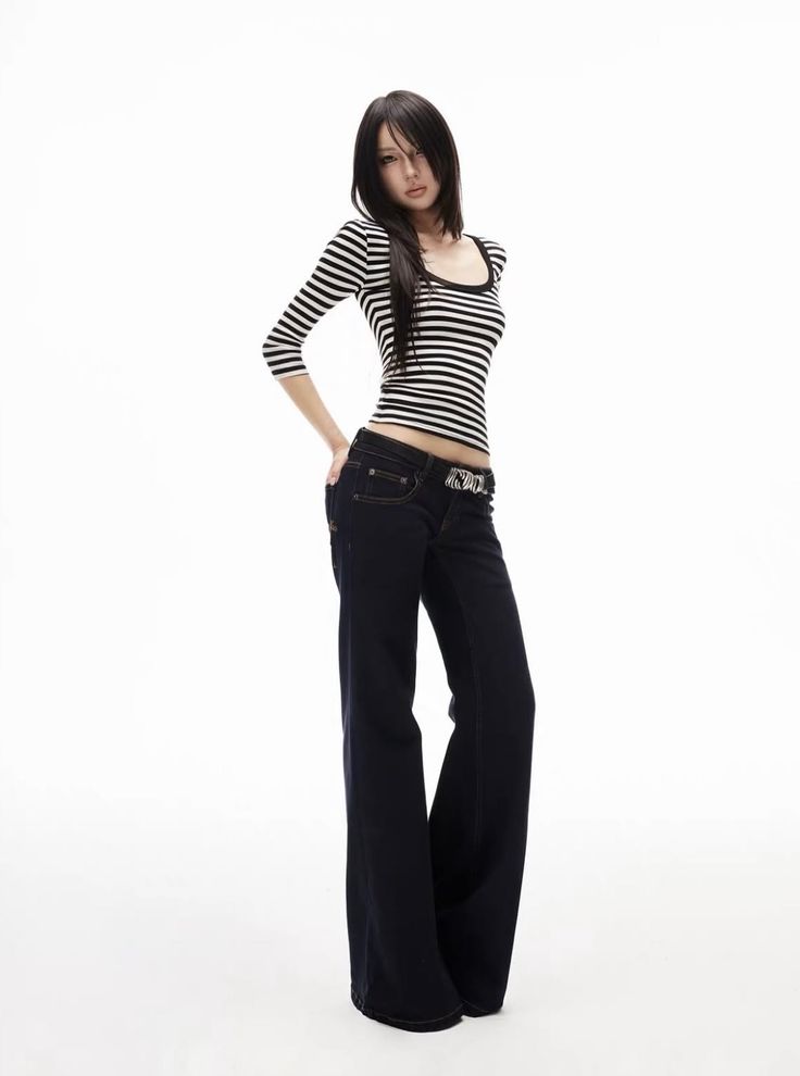 Woman with long black hair wearing a striped shirt and dark jeans in a studio