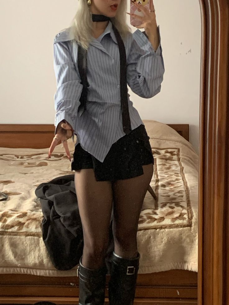 Person with blonde hair in a striped shirt, black shorts, and boots taking a mirror selfie