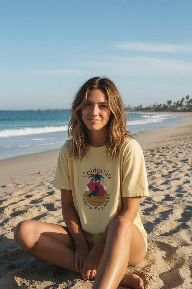 Woman with blonde hair sitting on a beach wearing a California themed t-shirt