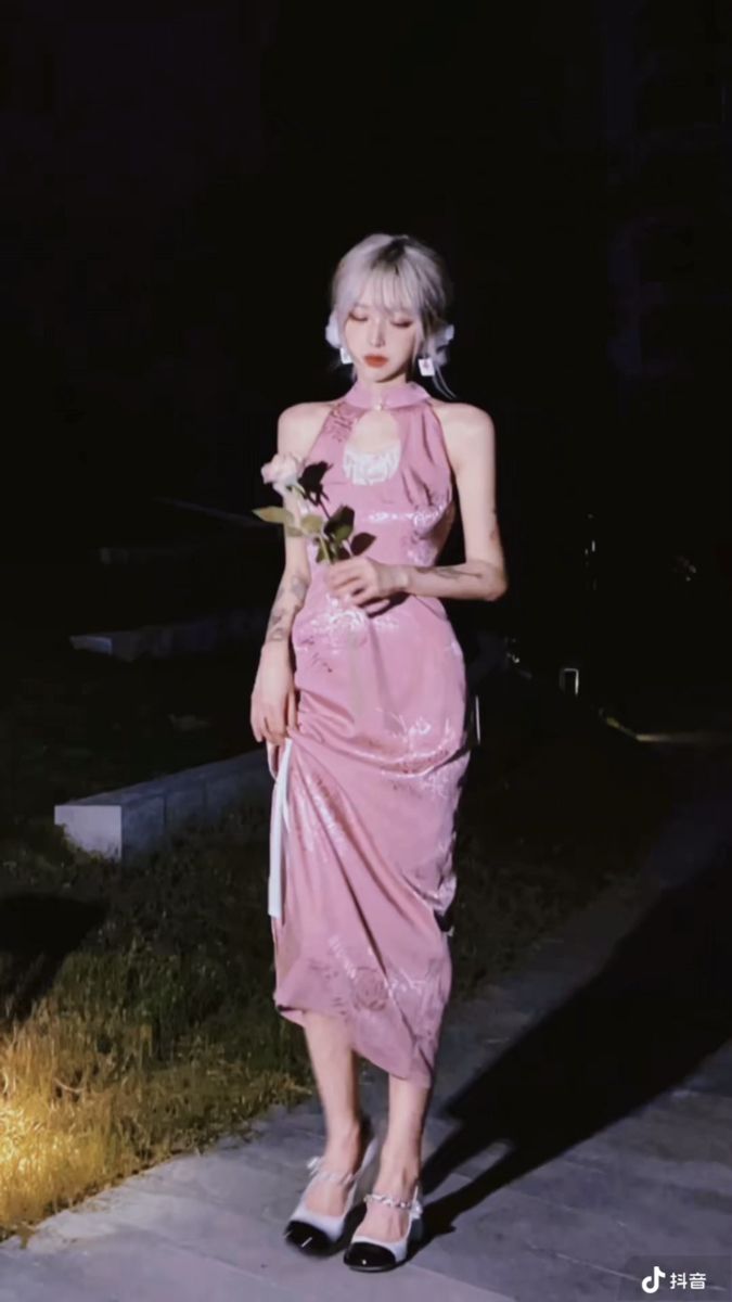 Woman in a pink halter neck dress holding a rose at night