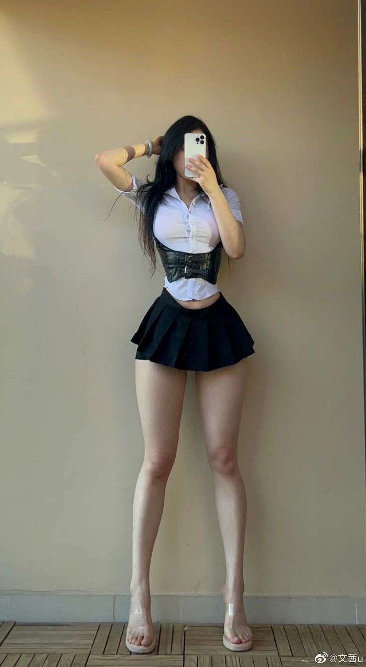 Woman in a white shirt, black corset, and mini skirt posing indoors