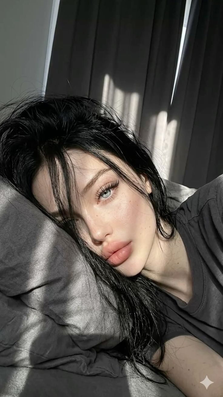 Woman with black hair and blue eyes lying on a pillow with sunlight stripes
