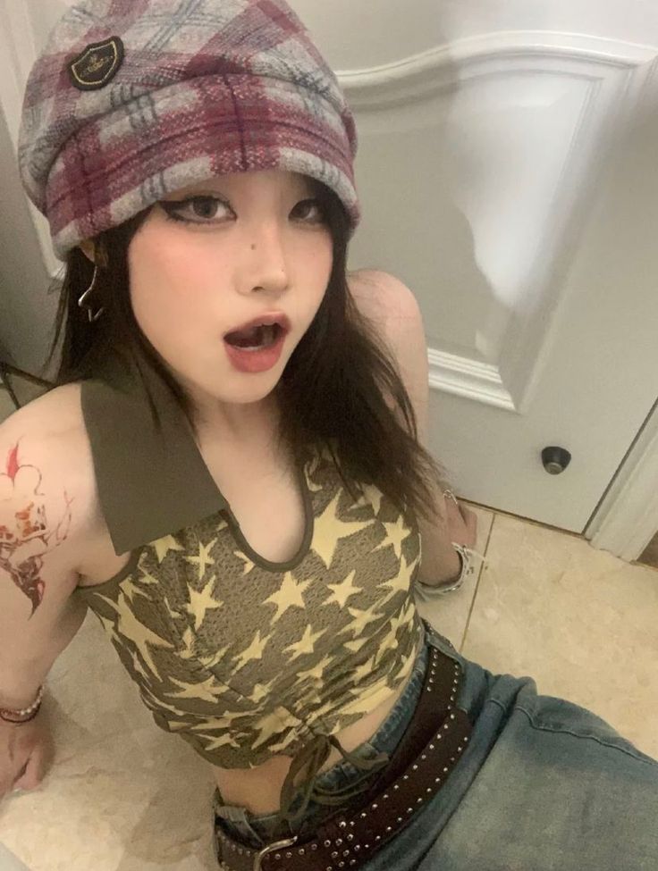 Woman in a plaid hat and star print top with a tattoo on her arm