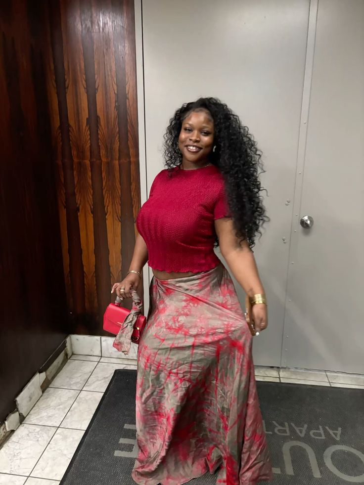 Woman with long curly hair in a red crop top and maxi skirt holding a red handbag