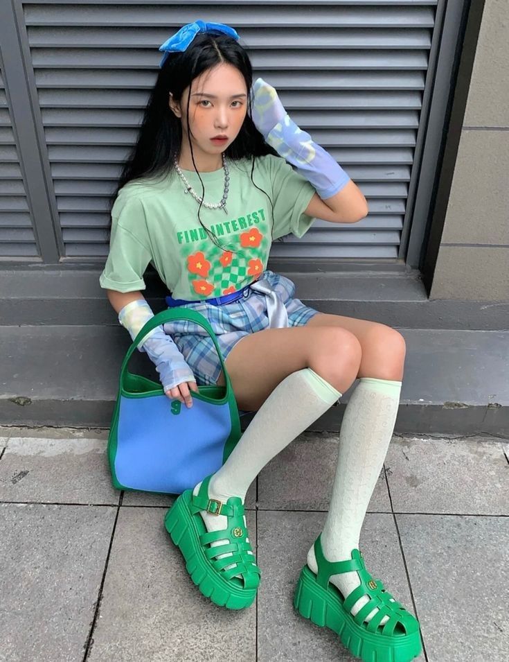 Woman with long black hair wearing a green t-shirt and plaid shorts, sitting outdoors