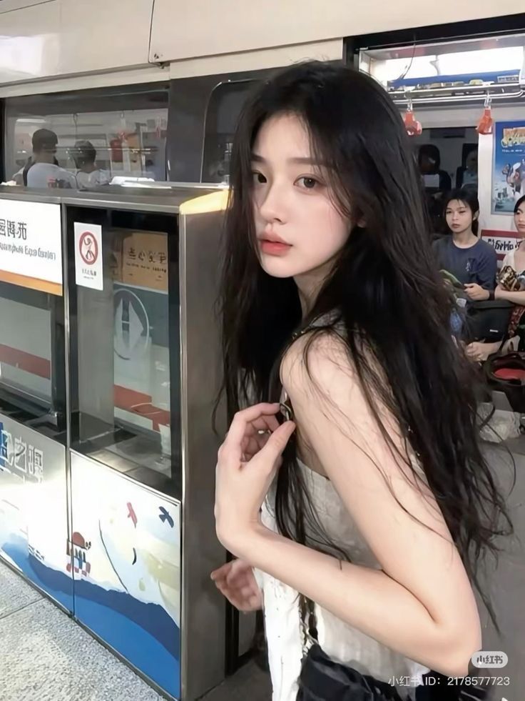 Woman with long black hair in a white top at a subway station