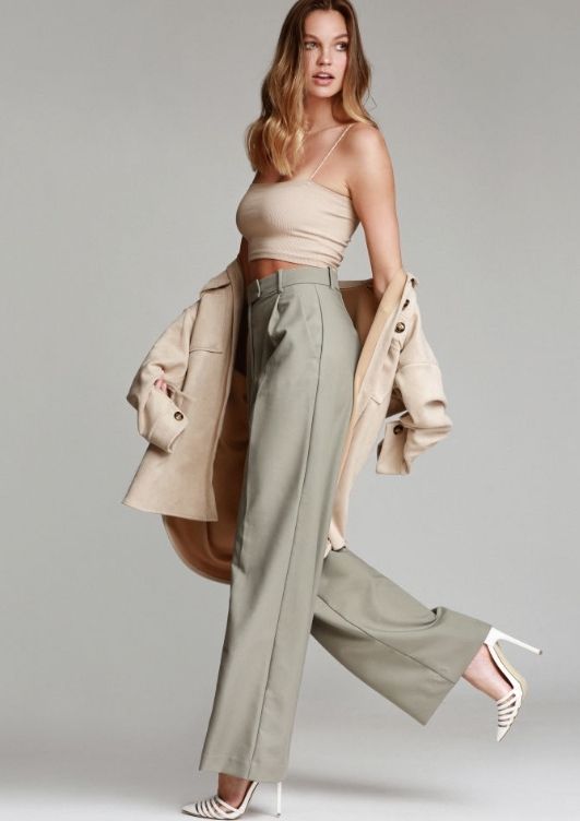 Woman in a crop top, wide leg pants, and a jacket over her shoulders