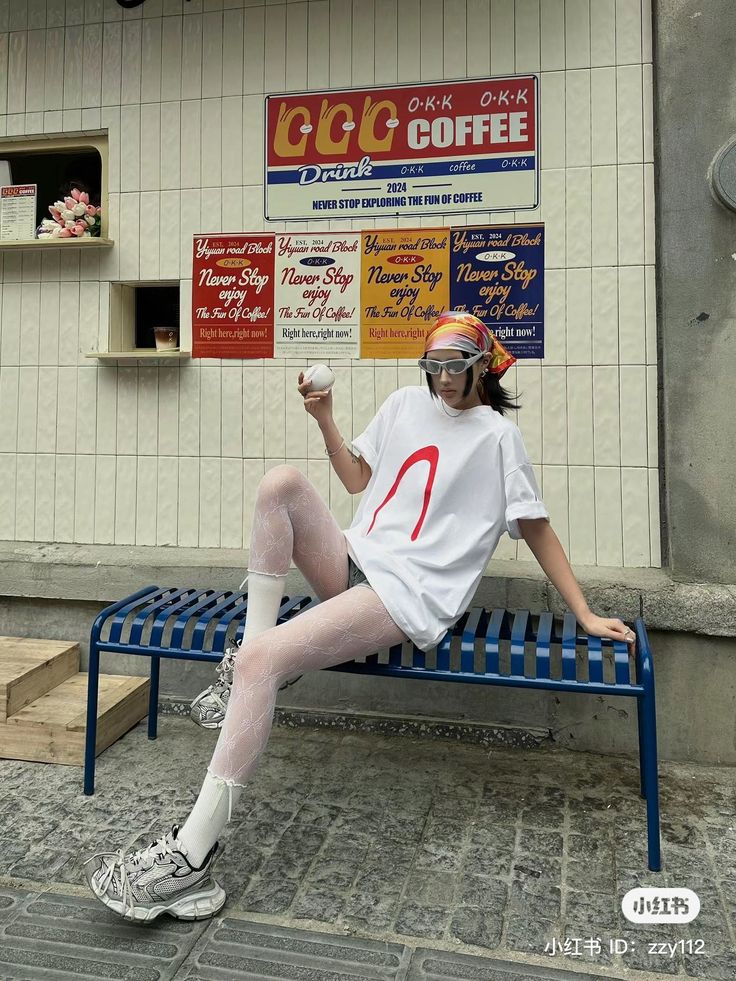 Person in a white t-shirt and patterned tights sitting on a blue bench outdoors