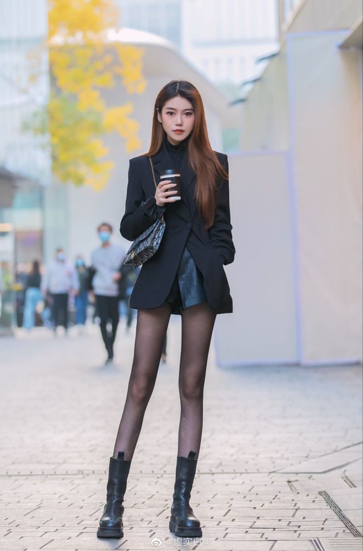 Woman in a black blazer and leather shorts holding a coffee cup on a street