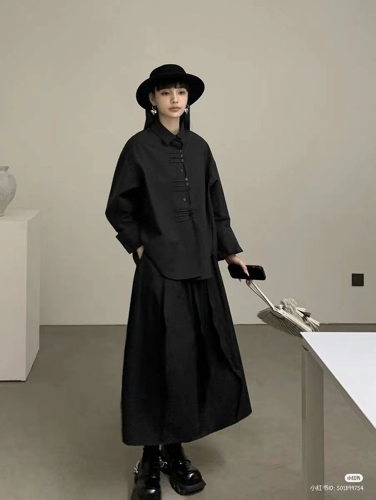 Woman in a black outfit with a hat and long skirt standing indoors