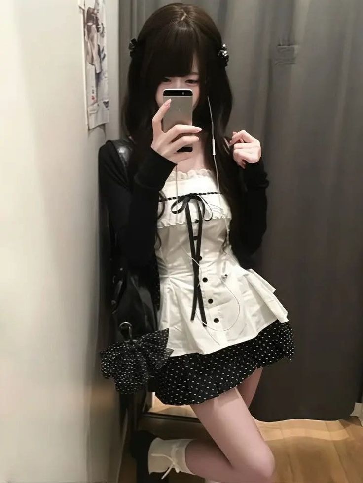 Woman in a maid-style dress and black cardigan taking a selfie indoors
