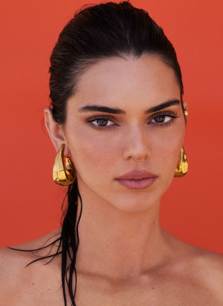 Woman with wet dark hair and gold earrings against a red background
