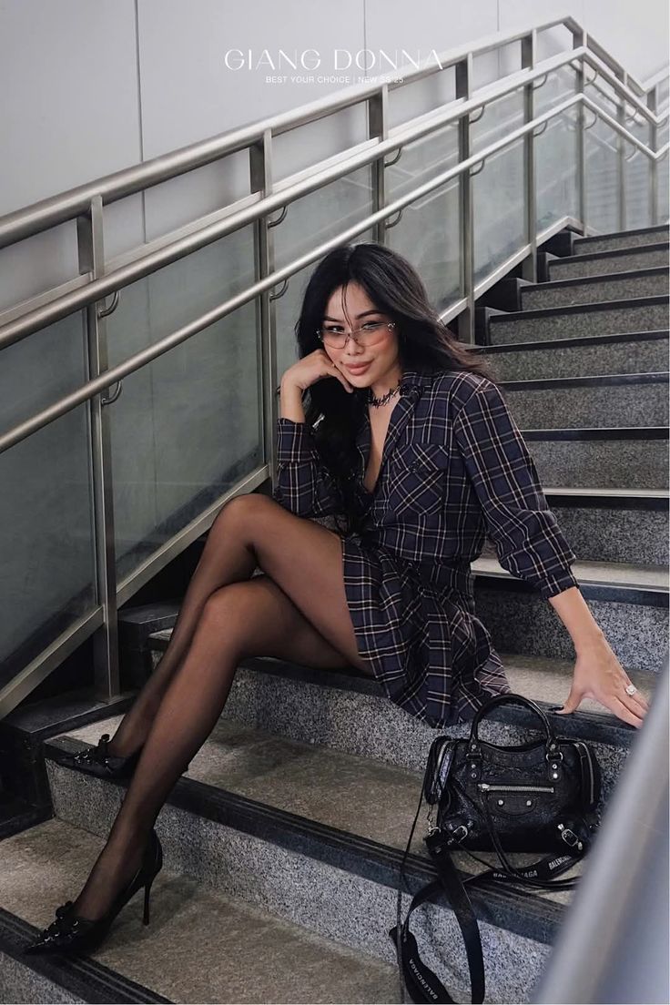 Woman in a plaid dress and black tights sitting on stairs indoors