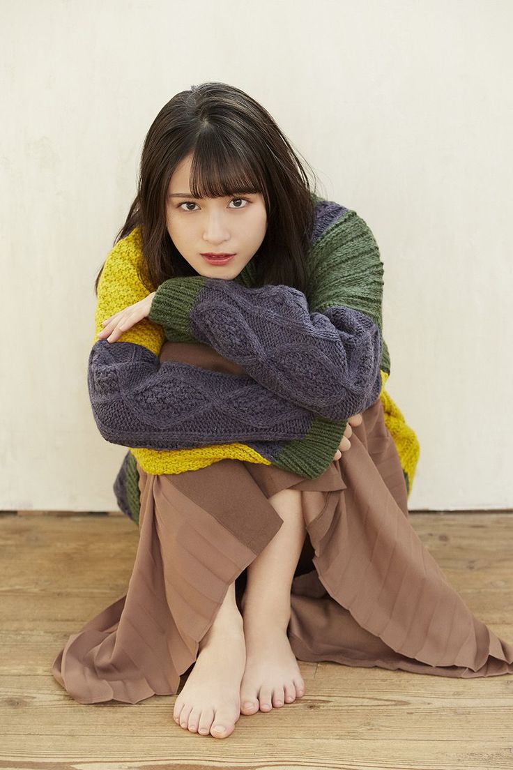 Woman with long hair wearing a colorful sweater and brown skirt, sitting indoors