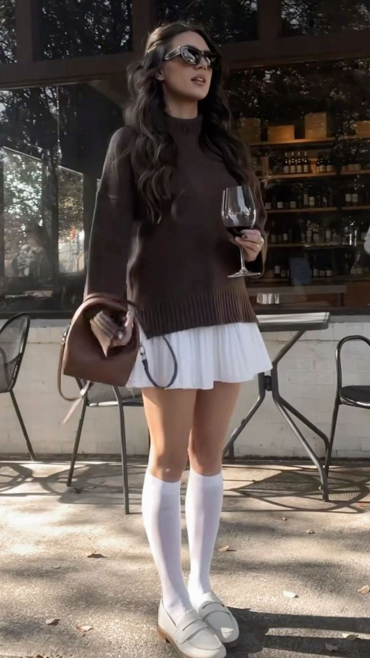 Woman in a brown sweater and white skirt holding a glass of red wine outdoors