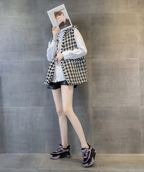 Person in a houndstooth vest and black shorts holding a magazine over their face