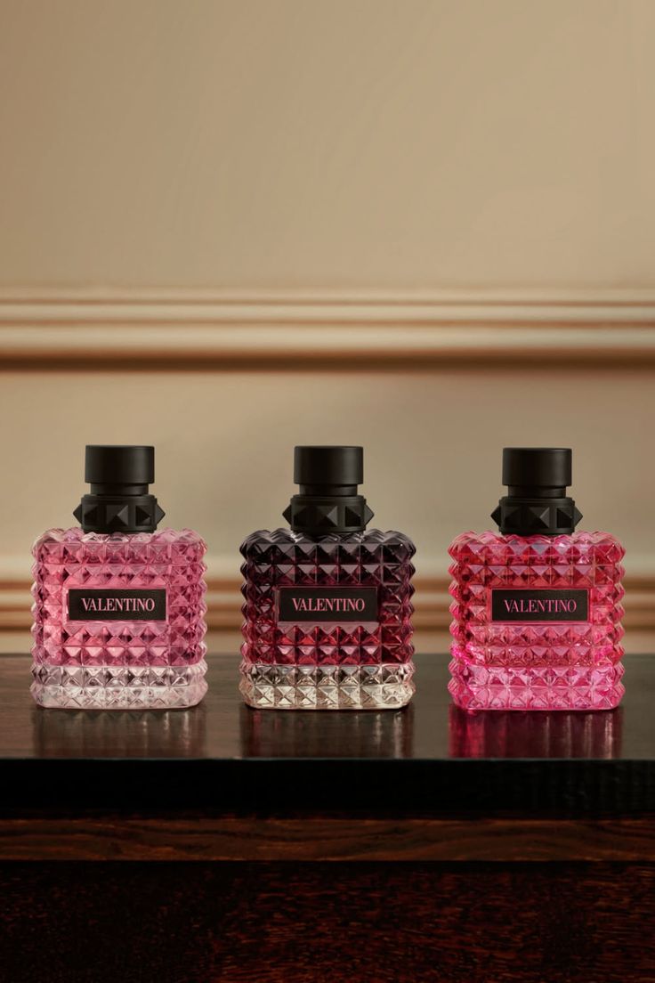 Three Valentino perfume bottles with studded caps on a dark wooden surface