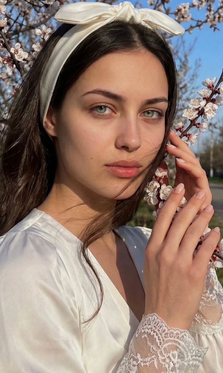 Woman with a white headband and green eyes holding a flowering branch
