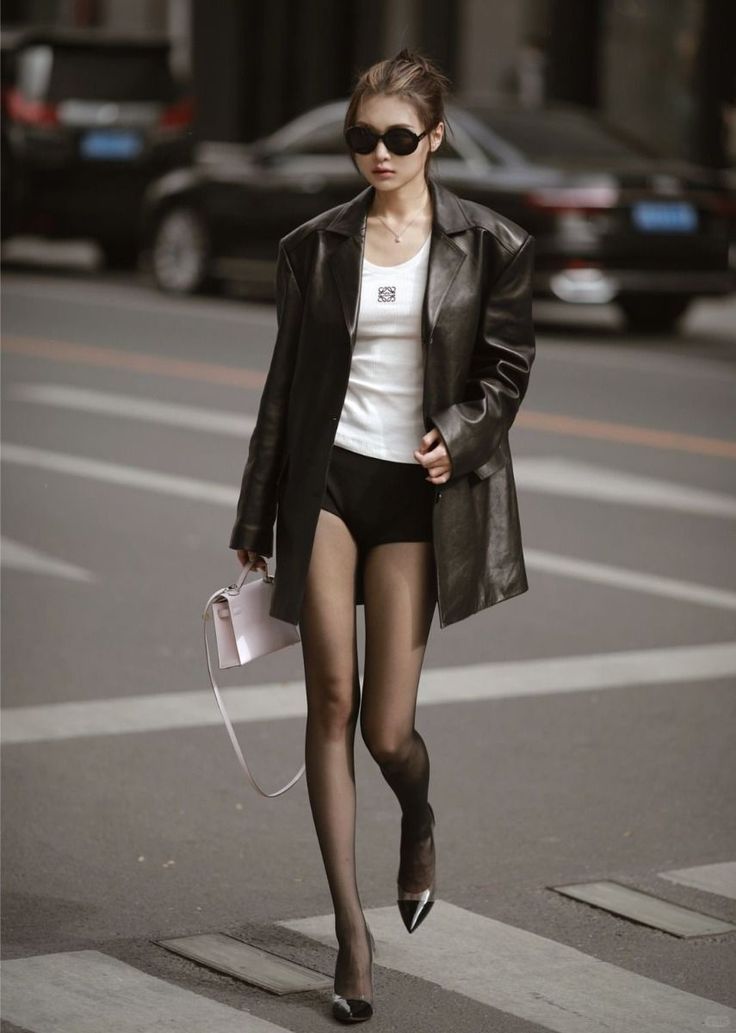 Woman in a leather jacket, black shorts, and tights walking on a street