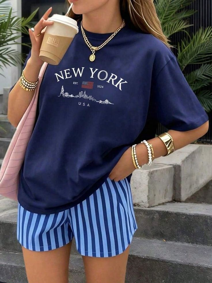 Person in a navy New York t-shirt and blue striped shorts holding a coffee cup