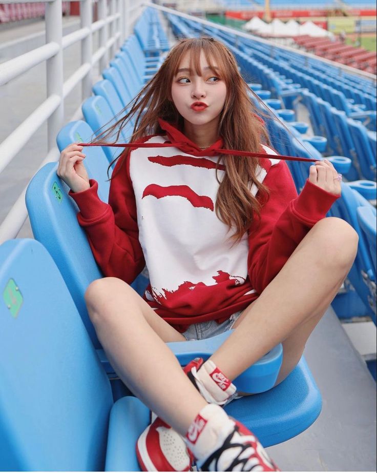 Woman in a red and white hoodie sitting on blue stadium seats