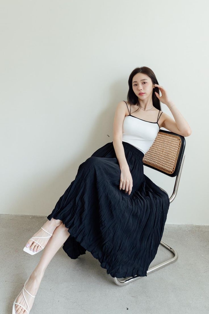 Woman in a white camisole and black maxi skirt sitting on a chair indoors