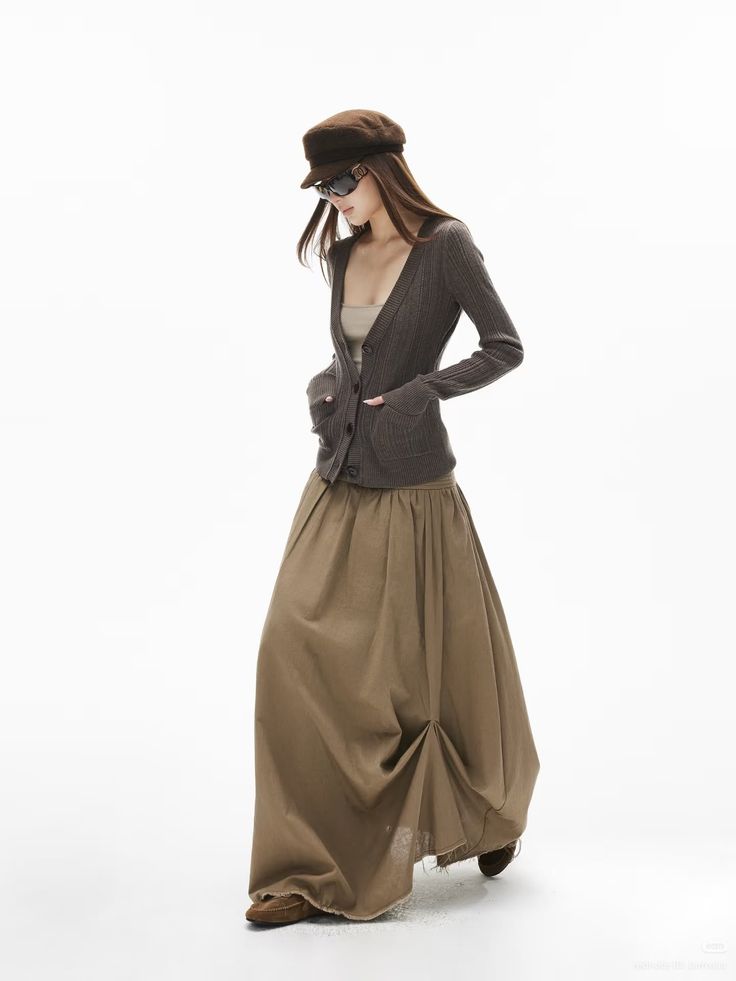Woman in a brown cardigan, maxi skirt, and hat posing in a studio