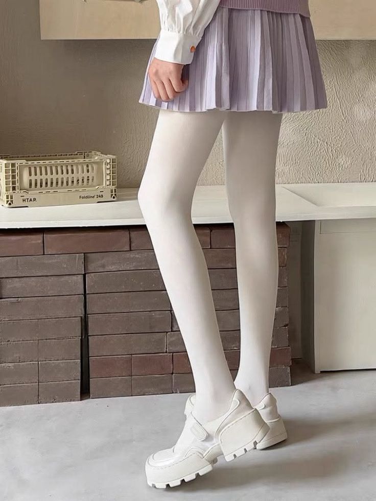 Person wearing a pleated skirt, white tights, and white shoes indoors