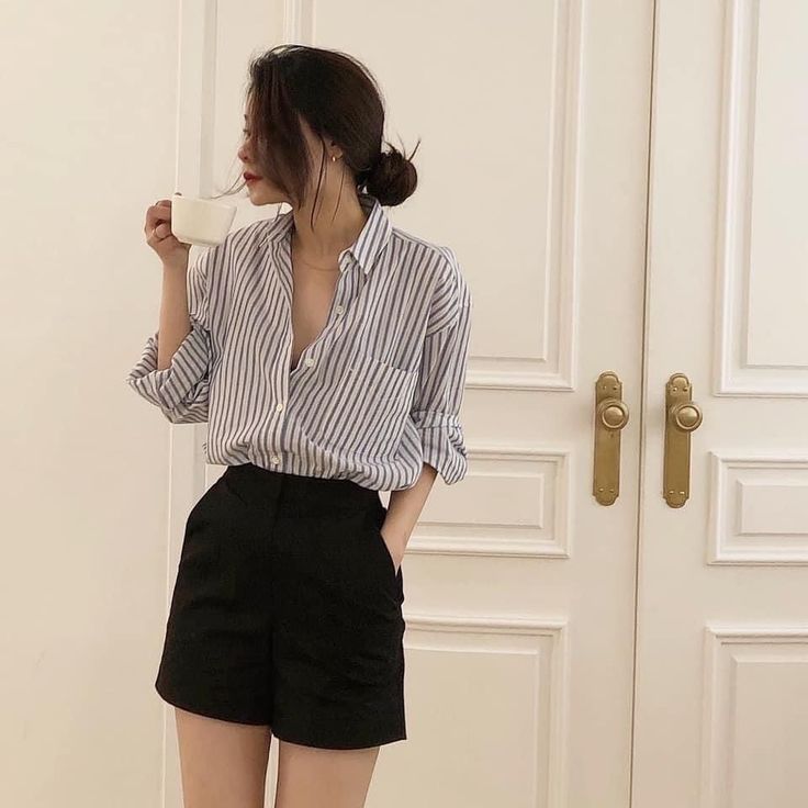 Woman in a striped shirt and black shorts holding a cup indoors