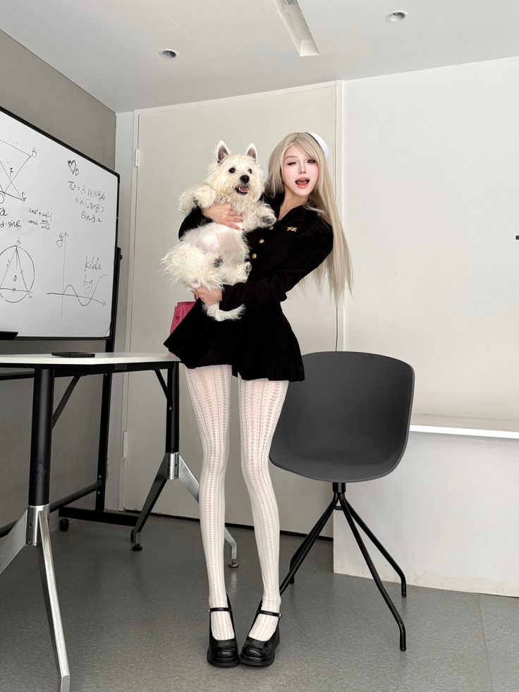 Woman with long blonde hair holding a white dog, wearing a black dress and white tights